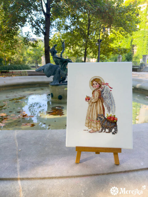 Siuvinys Merejka smėlio drobėje su angelu ir rakunu, ant mažo medinio stovo prie fontano, skirtas dovanai ar dekorui