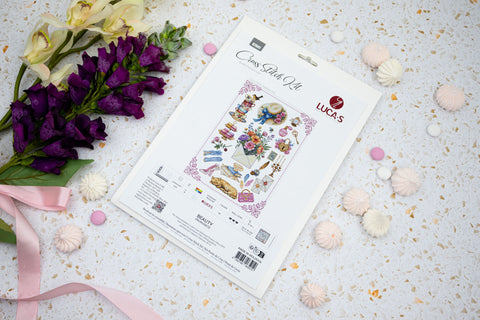 Kryželių rinkinys Beauty ant baltos kortelės pasvirusiu kampu, papuoštas violetinėmis gėlėmis ir saldainiais