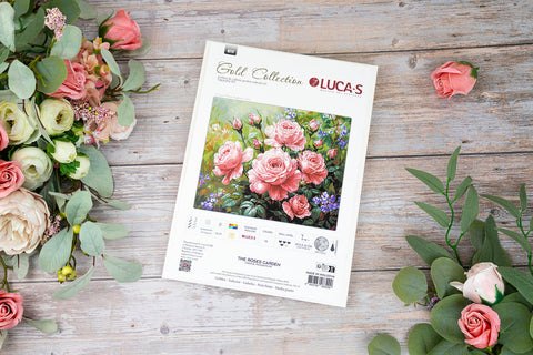Siuvinėjimo rinkinys LUCA‑S su rožių motyvu, baltame pakuotės viršelyje matomas spalvotas piešinys, plokščias viršaus kampo kompozicijos rodinys