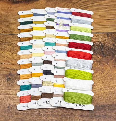 Siuvinėjimo siūlai LetiStitch — įvairių ryškių ir pastelinių spalvų kortelės, išdėstytos ant medinio fono