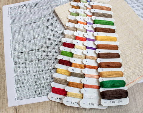Siuvinėjimo siūlai Letistitch spalvų paletė ant popierinės kryželių schemos su audiniu, žvelgiant iš viršaus
