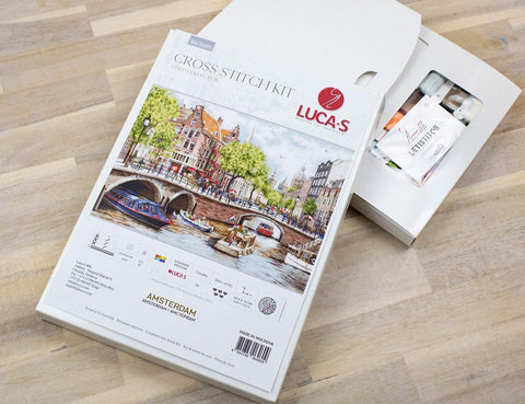 Kryželių rinkinys Lucas Amsterdam su paketu siūlų ant medinio stalo, matomas atidarytas pakuotės viršus