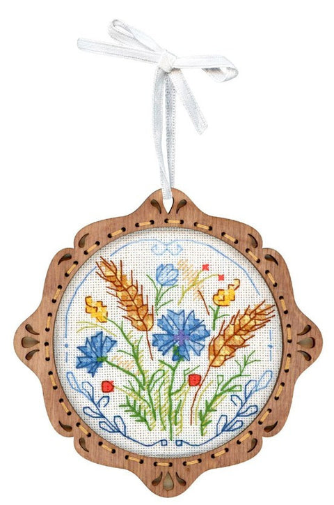 Siuvinėtas medinis ornamentas, apvalus rėmas su mėlynais žiedais, kviečių varpomis ir raudonomis smulkiosiomis gėlėmis, kabinamas balta kaspinu