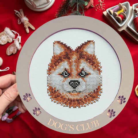 Siuvinys kryželiu: rudas ir baltas šuns veidas rėmelyje su graviruotu „Dog's Club“ žiedu, rodoma baigta versija