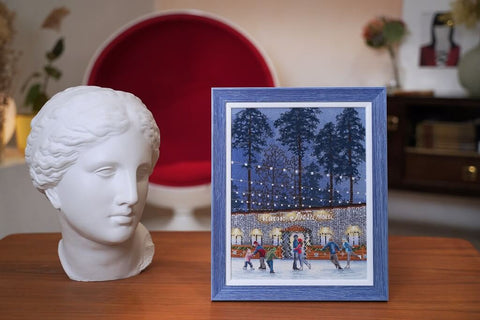 Rėmas su žiemos čiuožyklos paveikslu, melsvos medienos 20×25 cm, stovintis ant stalo priekinėje perspektyvoje