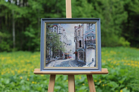 Paveikslas mėlyno rėmo, miesto gatvės siuvinėjimas 30×30 cm ant medinio molberto, artimas kampas parodo detalų tekstūrą