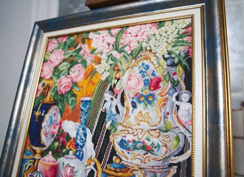 Siuvinėtas paveikslas (kryželiu), artimas kadravimas su gėlių ir ornamentuoto porceliano detalėmis, aukso rėmas