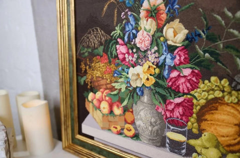 Siuvinėtas paveikslas gėlių kompozicija, aukso rėmas, rankų darbo kryželiu, kampinis artimas kadras su vaisiais ir žvakėmis
