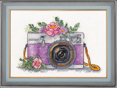 Siuvinėjimo rinkinys – baigtas violetinio fotoaparato kryželių paveikslas rėme su geltonu dirželiu ir rožiniais žiedais