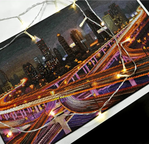 Miesto panoramos paveikslas naktinėje scenoje, oranžinės ir violetinės eismo šviesos, drobė 30×40 cm su pritvirtinta šiltai baltų LED girlianda