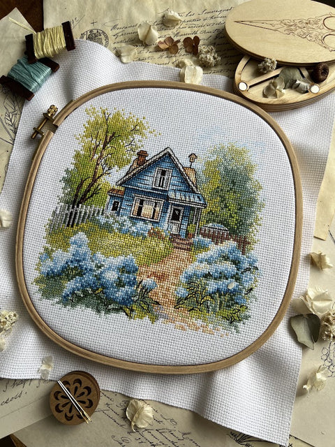 Siuvinėjimo rinkinys: mėlynas sodybos namelis kryželiu ant balto audinio 20×20 cm lankelyje su siūlų komplektu