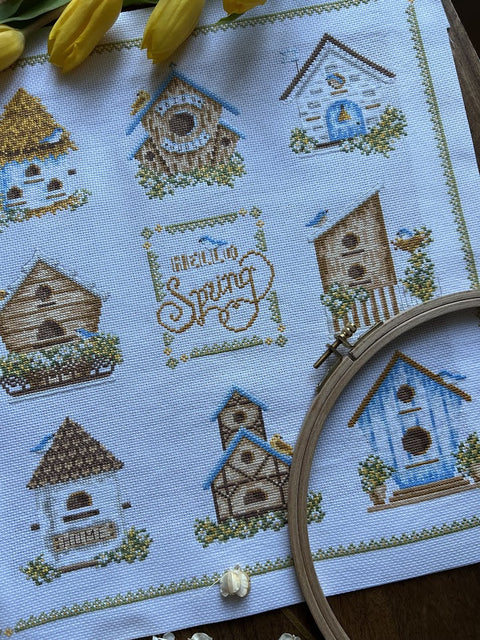 siuvinėta panelė su pavasario paukščių nameliais ant baltos drobės, rankų darbo siūlių detalės ir matomas siuvinėjimo lankelis