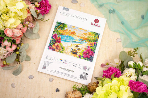 Kryželių rinkinys Lucas "Tropical Summer" ant pakuotės, parodytas iš viršaus šalia gėlių — priekis su paplūdimio piešiniu