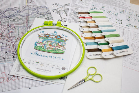Kryželių siuvinėjimo rinkinys Baby Carousel su žalia lankeliu, spalvotais siūlais, spausdinta schema ir mažomis žirklėmis.