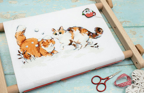 Siuvinėjimo rinkinys su rudais katinų motyvais ant baltos drobės, užfiksuotas ant medinio lankelio iš viršaus