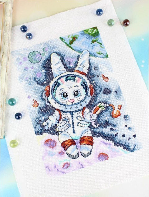 Kryželiu siuvinėjimo rinkinys: astronautinis triušis ant baltos drobės pastelinėmis spalvomis, detalus užbaigtas variantas