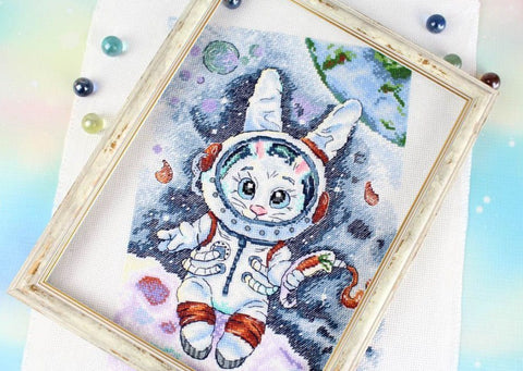 Kryželių siuvinėjimas rėmuotas – astronauto zuikio motyvas su pastelinėmis mėlyna–oranžinėmis spalvomis, kampinis artimas planas