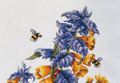 Siuvinėjimo rinkinys, artimas planas su violetinių ir oranžinių gėlių kryželių detalėmis ir dviem bitėmis, rodantis siūlių tekstūrą