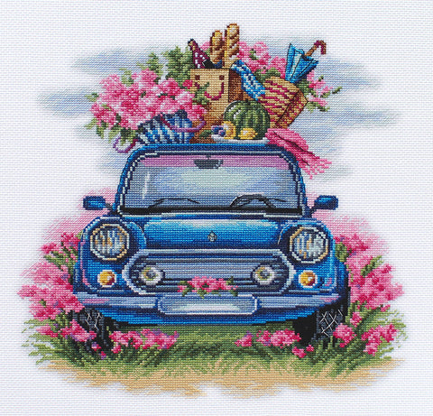 Siuvinėjimo rinkinys su mėlynu retro automobiliu iš priekio, ant stogo krepšys su duona, vaisiais ir skėčiu tarp rožinių gėlių, vasariška kompozicija
