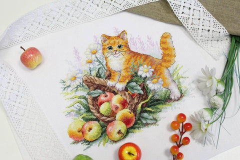 Kryželiu siuvinys su oranžiniu katinu ir obuolių krepšeliu ant baltos nėriniuotos medžiagos, pavasario motyvas