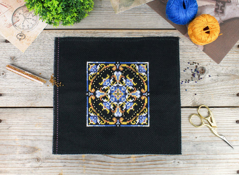 Siuvinys kryželiu ant juodos Aida drobės, 20×20 cm, geometrinis mėlynos ir aukso ornamentas centre, rankų darbo variantas