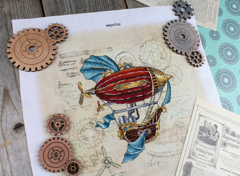 Kryželiu siuvinys: steampunk oro laivas raudonas su mėlynomis detalėmis ant smėlinio lino fono, plokščias kampinis vaizdas su mediniais krumpliais