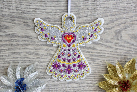 Kalėdinis angelas su sidabriniu blizgesiu, violetinėmis ir geltonomis siūlėmis bei raudona širdimi, pakabinamas baltu kaspinu