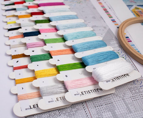 Siūlai Letistitch: spalvotų siūlų kortelės išilgai išdėstytos, arti matomas kryželių raštas ir siuvimo lankelis