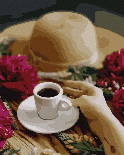 Espresso puodelis baltas porcelianinis artimas kadras su ranka šalia šiaudinės kepurės ir ryškių rožių