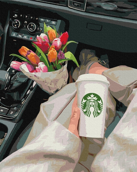 Starbucks puodelis baltas to go rankoje automobilio priekinėje sėdynėje šalia spalvotos tulpų puokštės