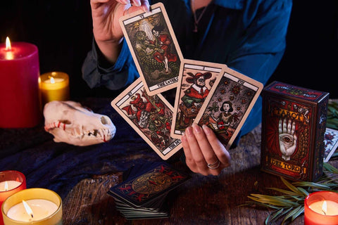 tarot kortos Del Toro, rankoje vėduojamos ir atskleidžiančios ryškias antikvarines iliustracijas, dekoratyvi dėžutė matoma šone