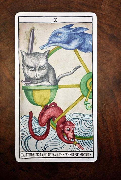 tarot korta Likimo ratas su pilku katinu, mėlynu triušiu ir raudona beždžione ant medinio fono