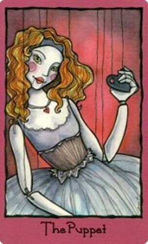 tarot korta The Puppet, iliustruota balta marionetė su rausvais skruostais ir raudonais plaukais, priekinė kortos pusė