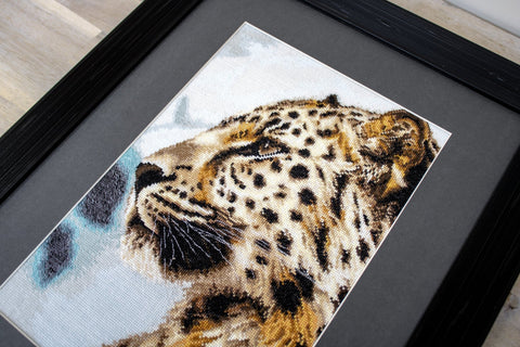 Siuvinėtas paveikslas leopardas, arti fiksuotas kampu ant juodo medinio rėmo, matomi detalūs kryželių stygų faktūra ir spalvų niuansai