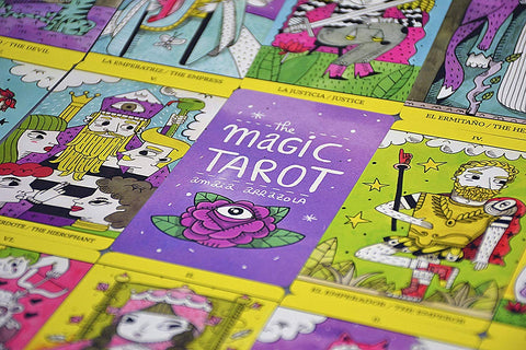 Tarot kortos The Magic Tarot su violetine dėkle ir ryškiomis, geltonu rėmeliu apvestomis didžiųjų arkanų kortelėmis, plokščiai išdėstytos