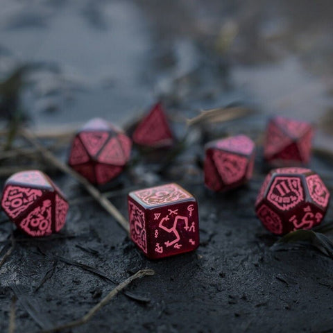 RPG kauliukai raudoni metaliniai rinkinys su įgraviruotais runų simboliais, arti padėtas kubas ant drėgnos juodos žemės