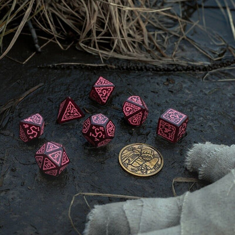 RPG kauliukai juodo korpuso su rožiniais raižiniais, 7 dalių rinkinys ant drėgno paviršiaus su auksine monetėle skalai