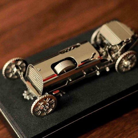 miniatiūrinis automobilis sidabrinis metalinis retro lenktyninis modelis ant juodo putplasčio stovo, matomas iš viršaus, akcentuojant ratus ir šasį