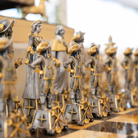 Šachmatai su sidabro ir auksu dengtomis muskietininkų figūrėlėmis, artimas kampinis planas, ryškios rankų darbo detalės