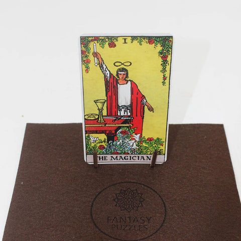 tarot korta The Magician stovi vertikaliai ant mažo medinio stovo ant rudos veltinio plokštelės su Fantasy Puzzles logotipu