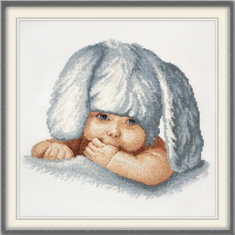Kryželiu siuvinėtas paveikslas – gulintis kūdikis su pilkomis triušio ausimis, baltas klasikiniu rėmu, apytiksl. 30×30 cm