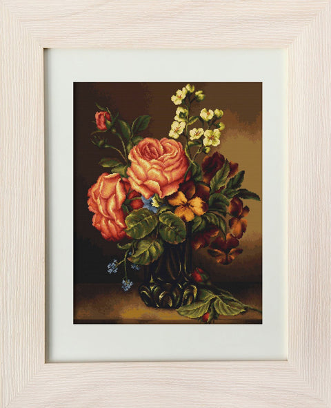 Kryželiu siuvinys smėlio spalvos rėme, rožinės ir geltonos gėlės vazoje, matomas iš priekio, šiltos spalvos ir tamsus fonas, tinkamas 40×50 cm sienai