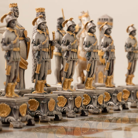 Šachmatai su sidabro ir aukso ornamentais, artimas priekinis kadras rodo karių figūrų ir raižyto pagrindo detales