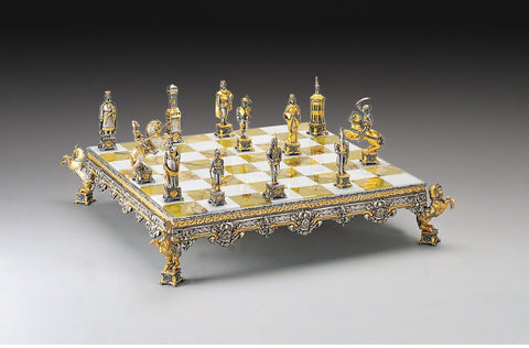 Šachmatai prabangaus aukso ir sidabro komplekto ant iškilotos dekoratyvios auksinės‑baltos langelių lentos, kampinė perspektyva