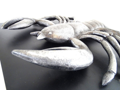 Metalinė skorpiono skulptūra sidabrine patina, arti parodytos priekinės žnyplės ir korpusas ant juodo pagrindo