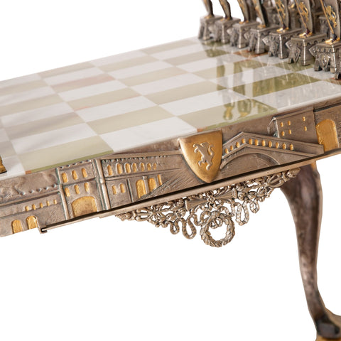 Šachmatų lenta iš marmuro su auksuotomis metalinėmis detalėmis, kampo artimas kadras pabrėžia ornamentuotą bortelį ir koją