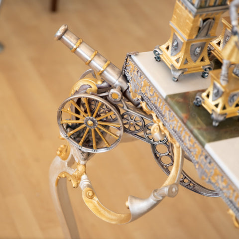 Stalas su aukso ir sidabro ornamentu: arti matomas dekoratyvus patrankos elementas ir rato detalė prie kampo