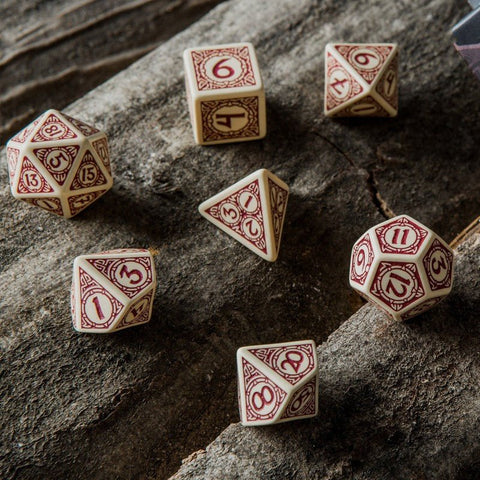 RPG kauliukai, kreminiai su raudonais ornamentiniais skaičiais, 7 dalių polihedrinis rinkinys ant akmens fono, artimas kampas