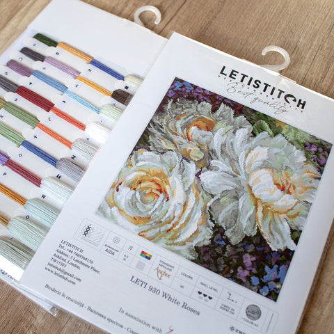 Kryželių rinkinys Letistitch White Roses su spalvota siūlų palete ir detaliu siuvinio raštu, matomas iš viršaus ant medinio fono