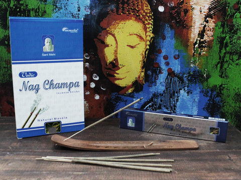 Nag Champa smilkalų lazdelės (Aromatika, mėlyna pakuotė) su mediniu laikikliu ir vienu degančiu smilkalų strypeliu prieš spalvotą Budos foną